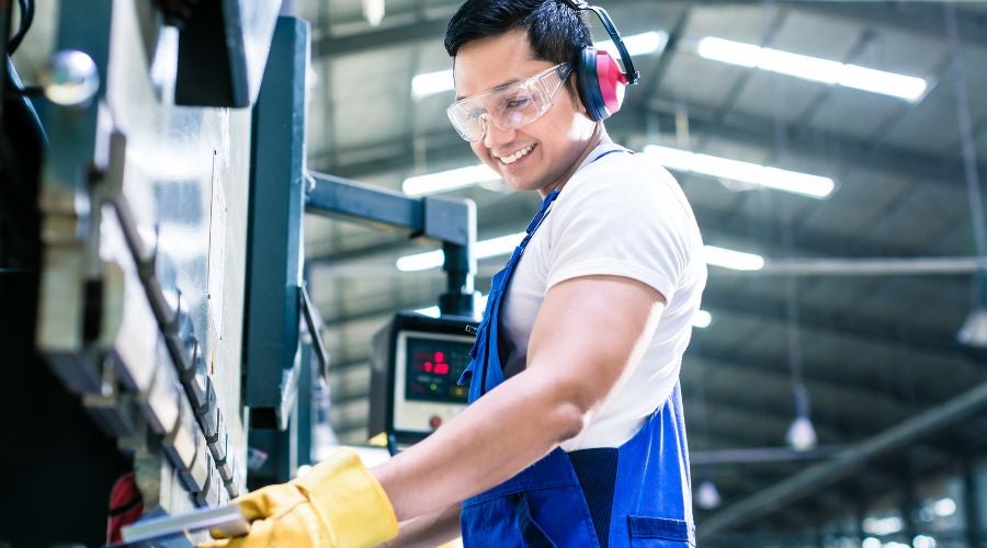 Man in blue overalls working with machinery in a factory.