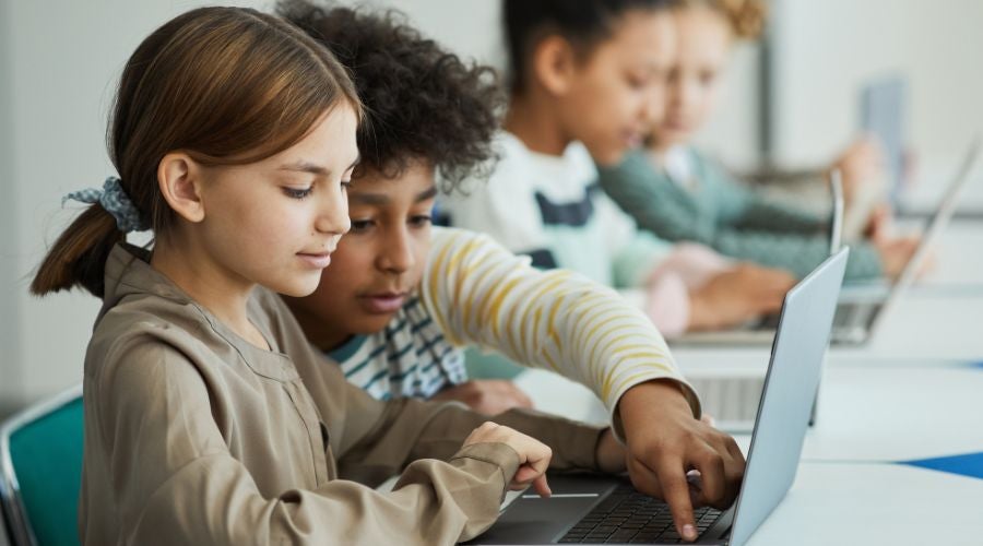Group of students using laptops in a classroom, collaborating on a project.